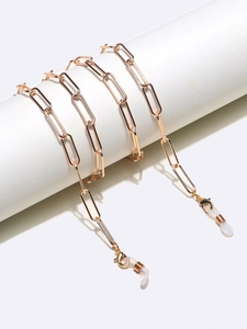 Detailed close-up of golden paperclip eyewear chain with silicone ends on white pedestal