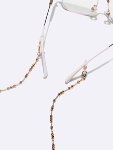 Golden metal beaded glasses chain with white silicone ends on a minimalist white surface