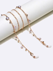 Détail de la chaîne à lunettes dorée avec perles mauves et strass sur support blanc