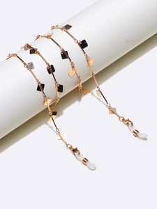 Detail of gold eyewear chain with black square pendants on a white column stand