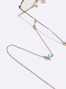 Detailed shot of golden eyewear chain with turquoise starfish charm on white background