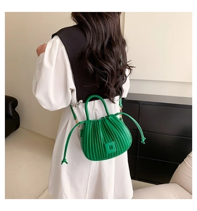 Detail showing the green pleated bucket bag worn as a crossbody with drawstring and buckle