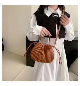 Detail of a brown pleated bucket bag showing vertical folds and round handle on a model