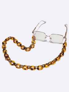 Détail d'une chaîne à lunettes en acrylique écaillé ambre sur monture dorée