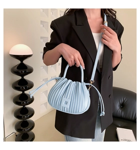 Detail of light blue pleated bucket bag with fine vertical texture and gold hardware
