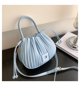 Close-up of light blue pleated bucket bag with leather texture and gold metal hooks