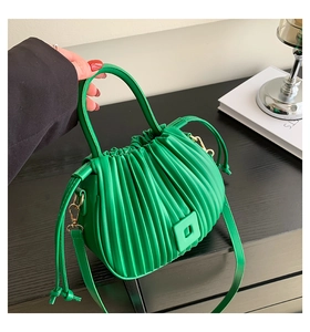 Detailed view of bright green pleated bucket bag with drawstring on black wooden table