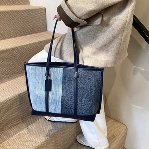 Détail du sac fourre-tout en denim bleu et cuir à grande capacité tenu par le mannequin