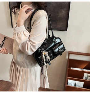 Detail of black glossy shoulder bag with functional pockets and a cute bear charm