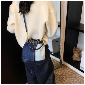 Detail of denim patchwork bucket bag with drawstring closure and metal eyelets on the shoulder strap