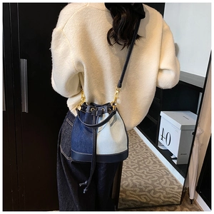 Detail of a denim bucket bag with navy leather trim and adjustable gold shoulder buckle