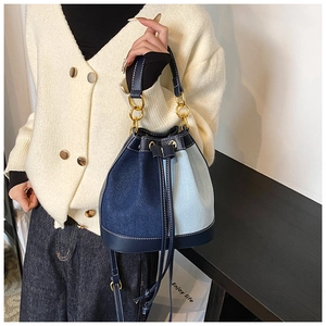 Detail of denim bucket bag with dual-tone patchwork and gold metal chain handle
