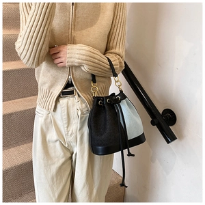 Detail of denim and black leather bucket bag showing textured fabric and drawstring closure