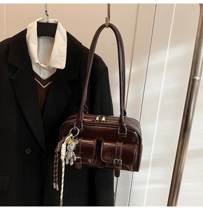 Detail of dark brown glossy underarm bag with double front pockets and silver bear charm