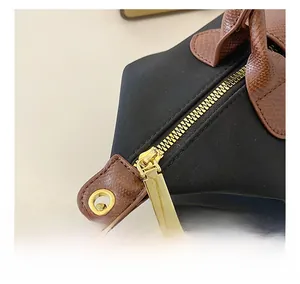 Detail of smooth gold zipper and brown pebbled leather trim on black nylon tote bag