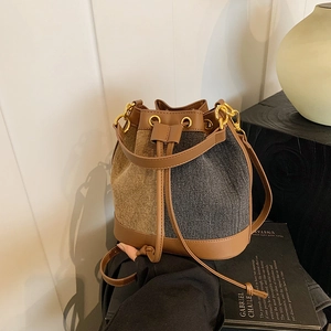 Detail view of denim bucket bag with contrasting leather trim and gold hardware rings