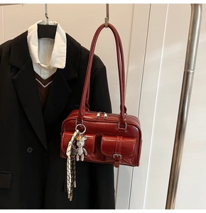 Detail view of a dark red glossy shoulder bag with twin pockets and a cute bear charm