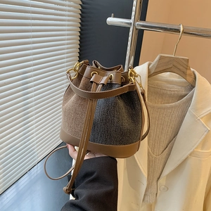 Detail of tweed bucket bag showing brown leather trim, drawstring, and metal hardware