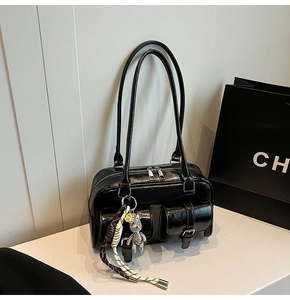 Close-up of black glossy leather Boston bag with silver hardware and bear pendant