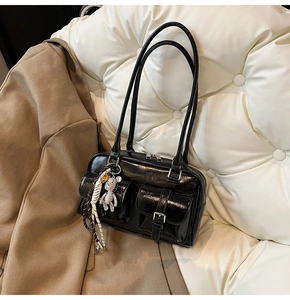 Detail of a black glossy underarm bag with multi-pockets, silver hardware and a bear charm
