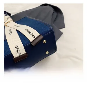Detail of dark blue denim tote with golden metal feet and decorative branded webbing
