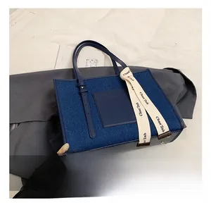 Detail of large denim tote bag showing leather handles and beige decorative ribbon