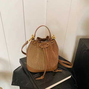 Detail of a brown drawstring bucket bag with textured fabric and leather trim details