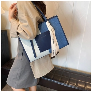 Detail of blue and white patchwork denim tote bag with leather pocket and decorative ribbon