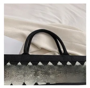 Detail of sturdy woven handles on a knit tote bag with black and white diamond patterns