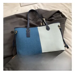 Detail of color-block denim tote bag with leather handles and gold metal hardware