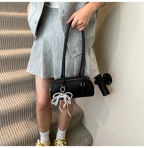 Detail of black pebbled leather Boston bag with white lace bow and pearl charm