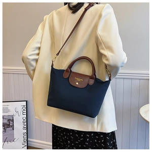Navy nylon crossbody bag with brown leather strap worn by a model in a blazer