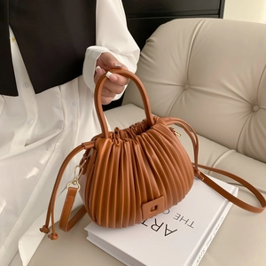 Brown pleated bucket bag with gold hardware on a white book, crossbody style