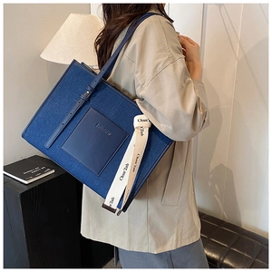 Detail of blue denim tote bag with leather pocket and decorative branded ribbon strap