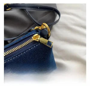 Close-up of golden zipper hardware and D-ring on denim tote bag with contrast stitching