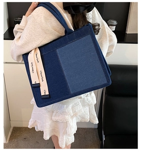 Detail of blue patchwork denim tote bag with side strap branding shown on a model