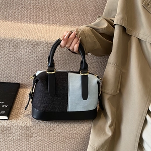 Fashionable denim and black leather patchwork handbag with gold buckles in bowling bag style
