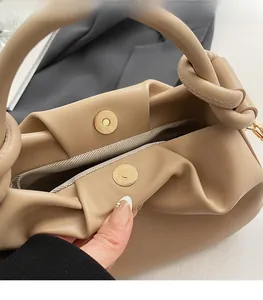Close-up of khaki pleated bucket bag featuring round magnetic buckle and knot handle detail