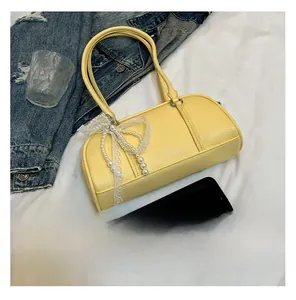 Detail of yellow baguette bag featuring lace and pearl bow charm on white fabric