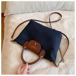 Detail of dark blue nylon tote with brown leather flap and golden metal hardware