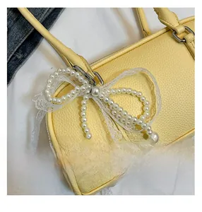Detail of yellow lychee leather handbag with pearl bow and lace accents