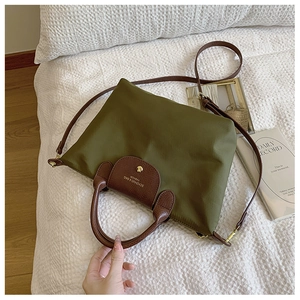Detail view of olive nylon tote with leather handles and gold snaps on a white bed