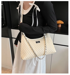Detail of beige pleated shoulder bag featuring vertical texture and silver chain strap