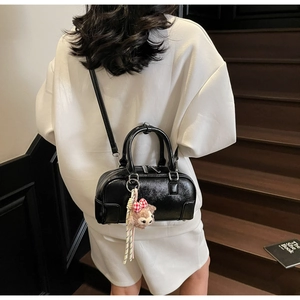 Close-up of black glossy cylinder bag with sleek shoulder strap and plush charm detail