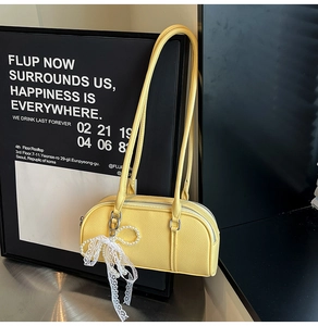 Close-up of yellow leather Boston bag with pearl chain and lace bow charm detail