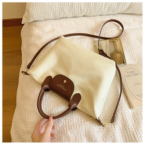 Close-up of cream nylon tote bag featuring brown leather flap and golden buckle detail