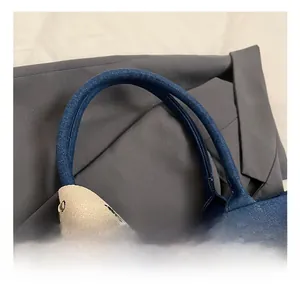Detailed close-up of dark blue denim tote handle with beige patterned ribbon strap