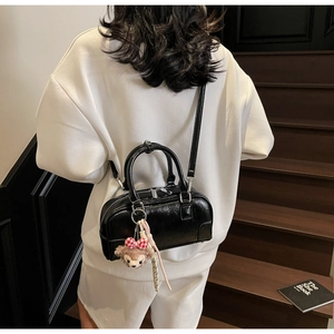 Detail of black glossy Boston bag with a plush charm on dark wooden stairs background