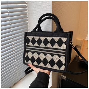 Detail of checkered tote bag with woven texture, striped center strap and black handles