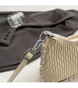 Detail of silver chain hardware and pleated leather texture on cream-white shoulder bag